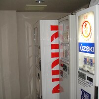 Máquina expendedora con un logotipo rojo llamativo, un dispensador de bebidas y un letrero con texto en japonés.