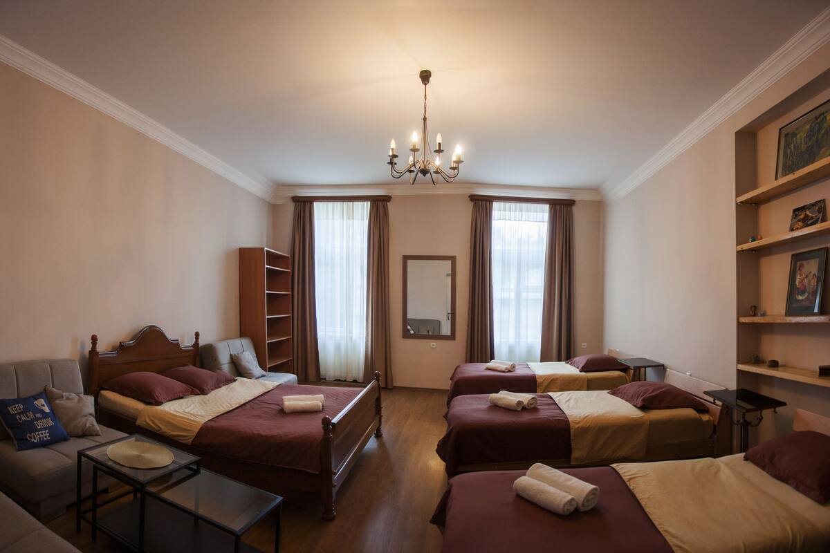 A hotel room with two beds, a sofa, a small table, a mirror, and a chandelier.