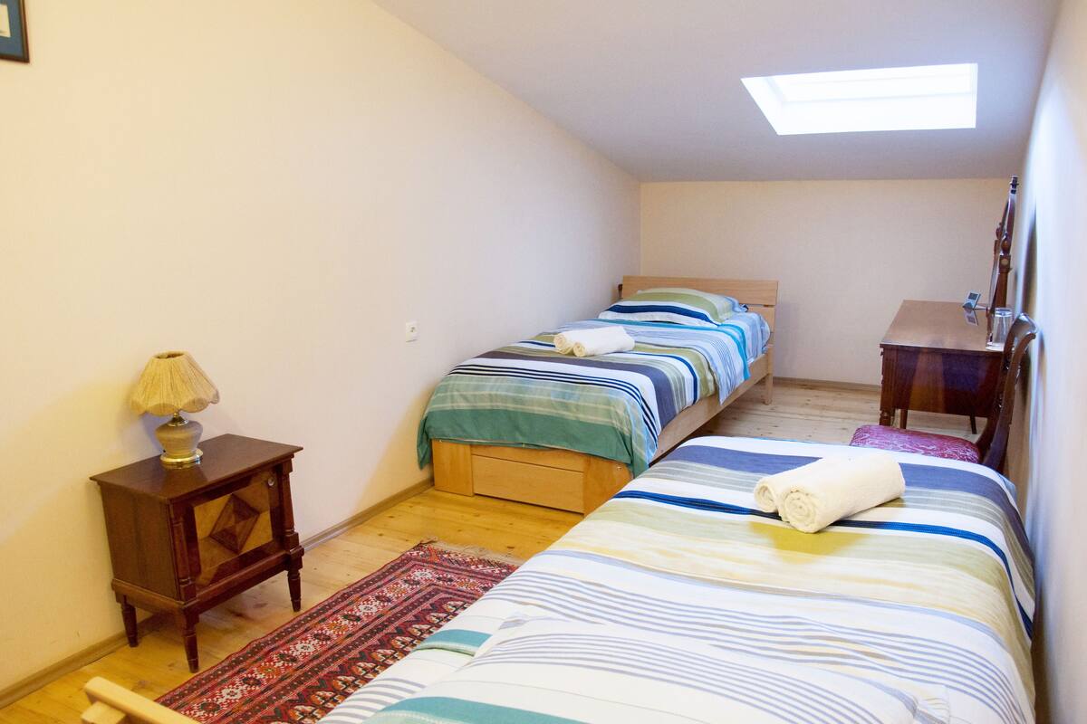 A small, cozy bedroom with two beds, a nightstand, a lamp, and a wooden dresser.