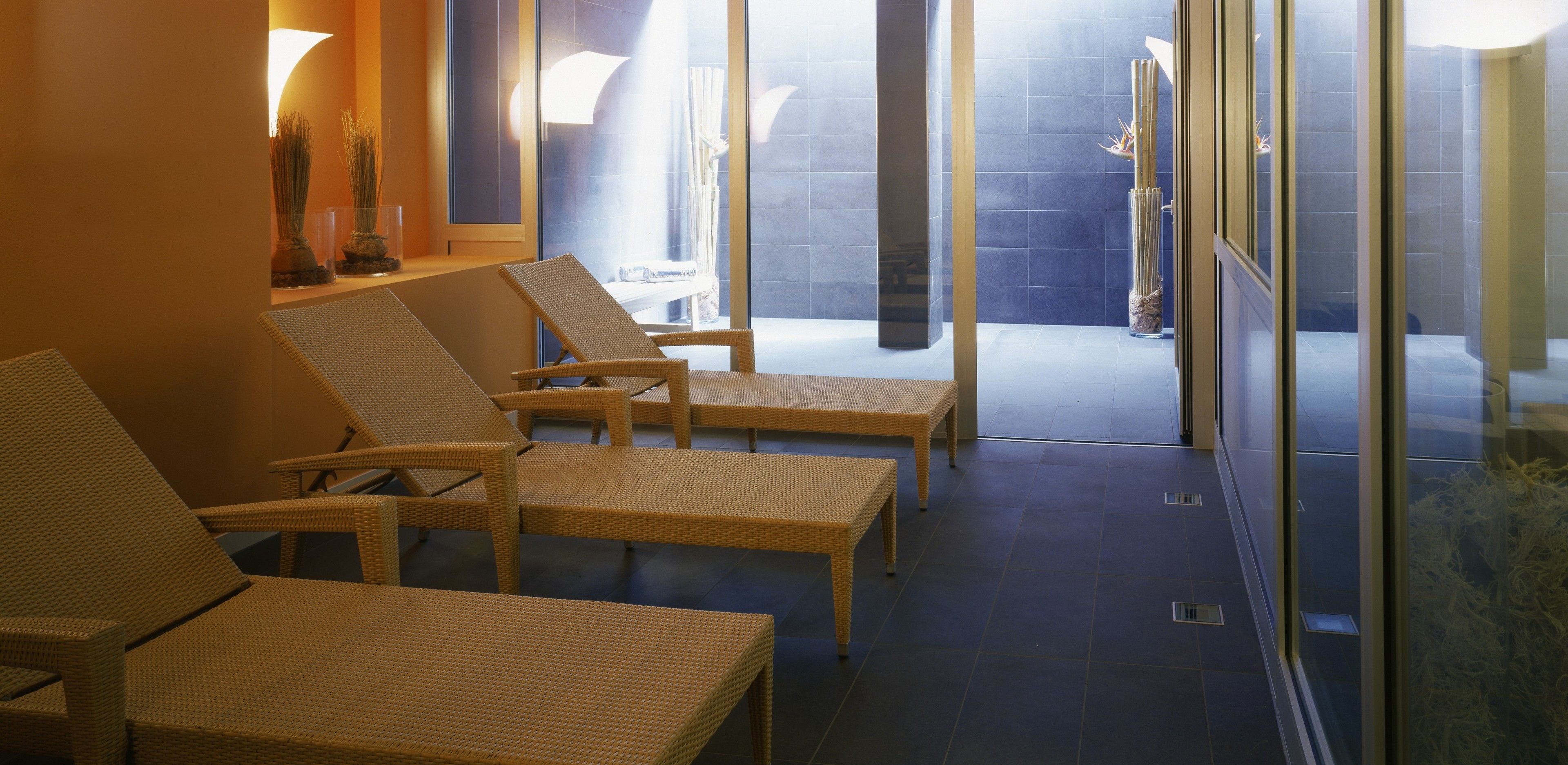 Espaço de spa com cadeiras de descanso de vime e parede de vidro que dá para um banheiro.