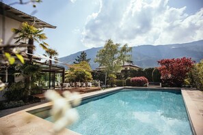Una piscina con zona de patio, rodeada de palmeras y vistas a la montaña.