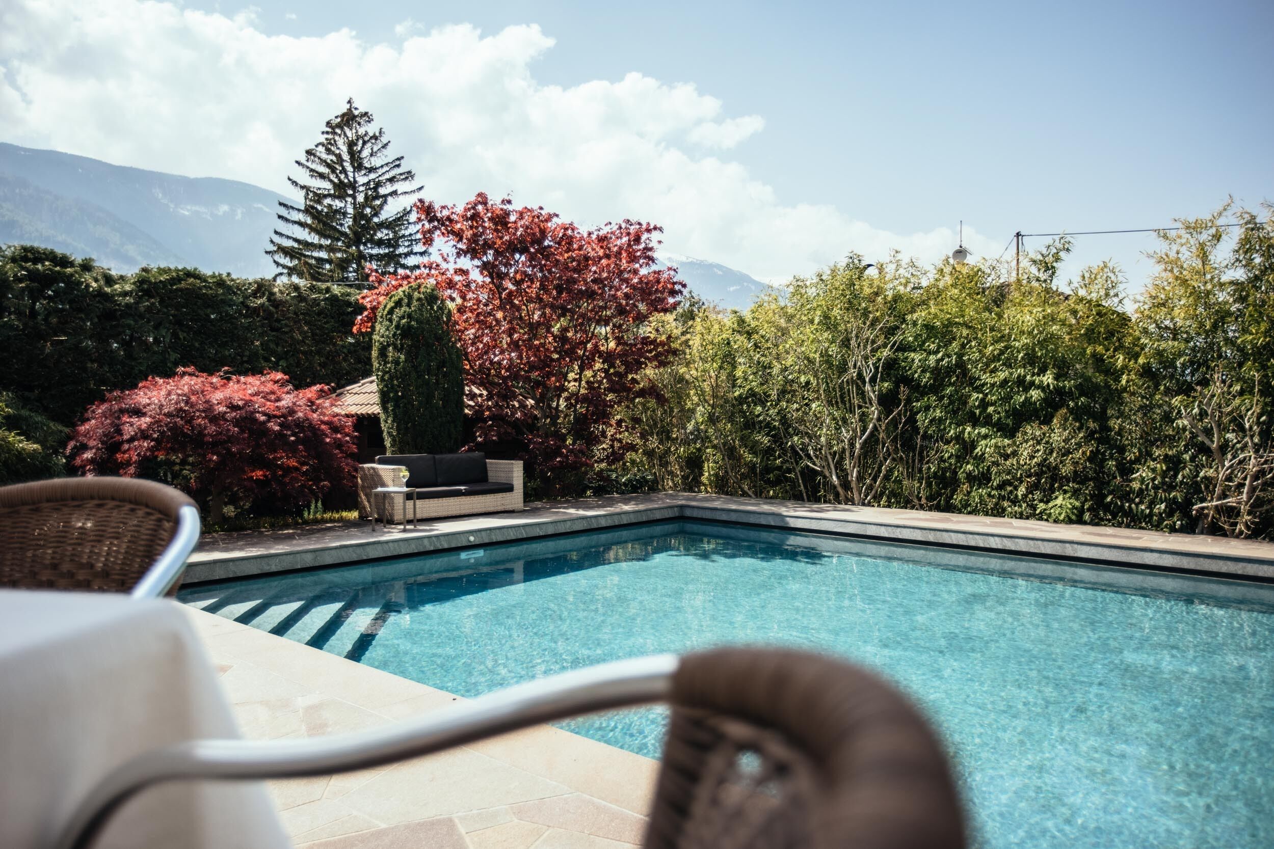 Ein Swimmingpool mit Blick auf Berge, umgeben von üppiger Vegetation und einer Terrasse mit Sitzgelegenheiten.