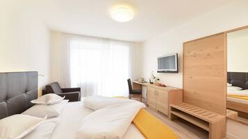 Ein Hotelzimmer mit Bett, Schreibtisch, Stuhl, Fernseher und Holzschrank.