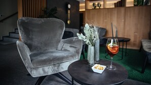 A modern living room with a grey velvet armchair, a round table with a drink and a small plate, and a decorative vase with flowers. - Hotel Rablanderhof (Parcines)