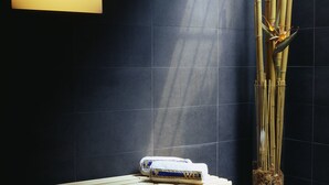 A bench with a towel and a water bottle, a tall bamboo plant in a vase, and a wall-mounted light fixture. - Hotel Rablanderhof (Parcines)