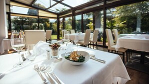 A dining area with tables set for a meal, featuring a glass enclosure and a view of the outdoors. - Hotel Rablanderhof (Parcines)