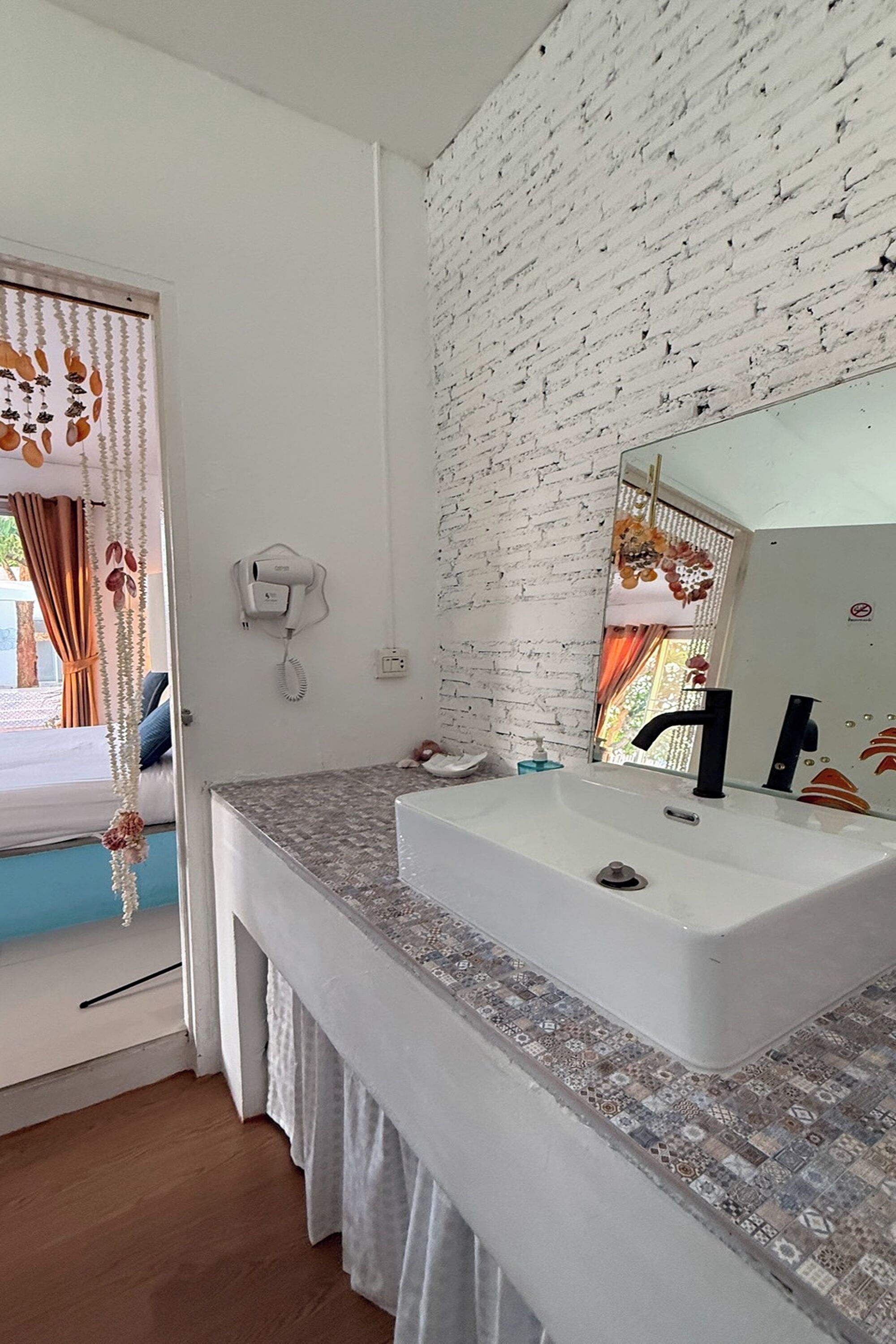 A bathroom with a white sink, a mirror, a hairdryer, and a window with curtains.