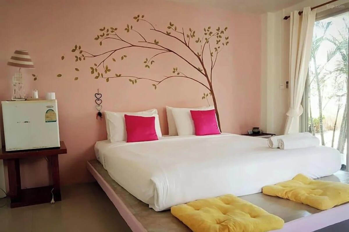 A bedroom with a bed, pillows, a bedside table, a lamp, and a wall decoration.