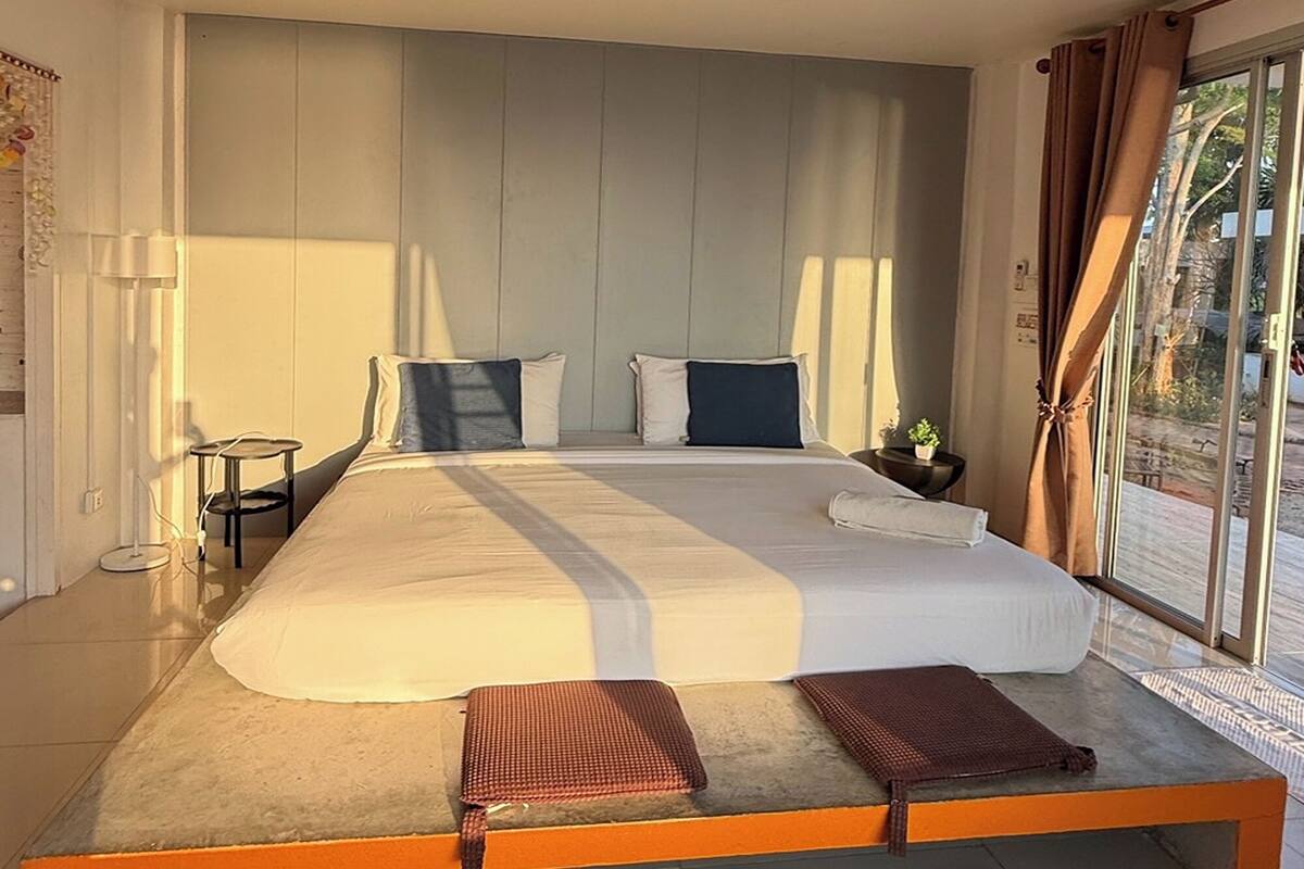 A modern bedroom with a large bed, a small bedside table, and a view through a glass door.