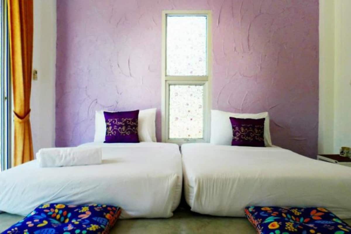 A room with two beds, a window, and a view of greenery outside.