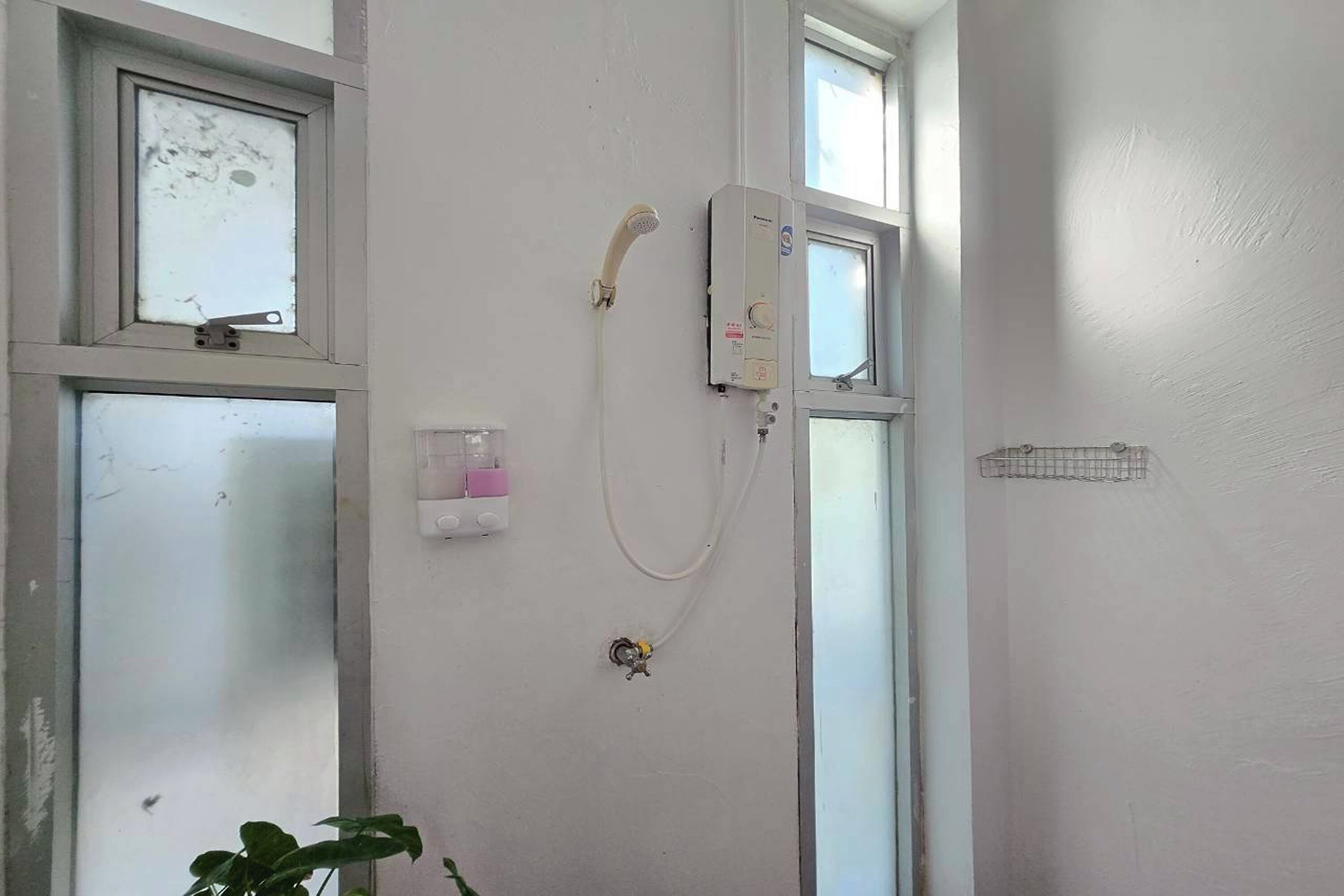 A bathroom with a shower, a window, and a wall-mounted electrical box.