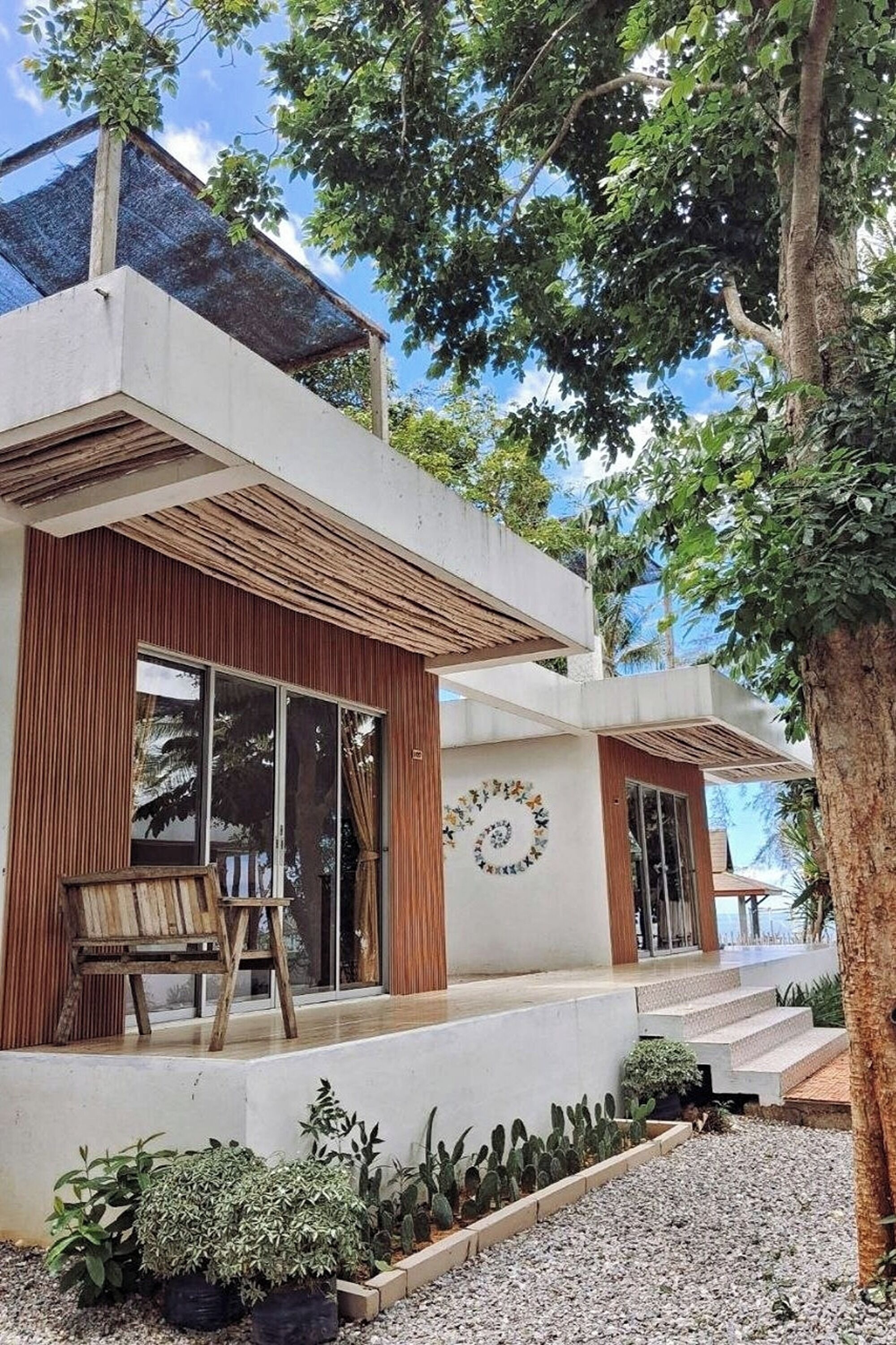 Uma casa moderna com uma janela grande, um banco de madeira e um jardim com diversas plantas.