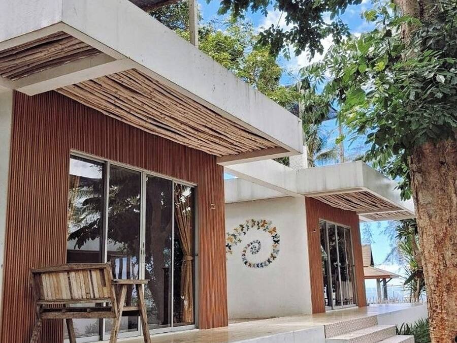 Uma casa moderna com uma janela grande, um banco de madeira e um jardim com diversas plantas.