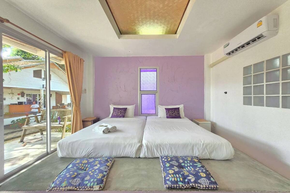 A room with two beds, a large window, and an air conditioning unit.