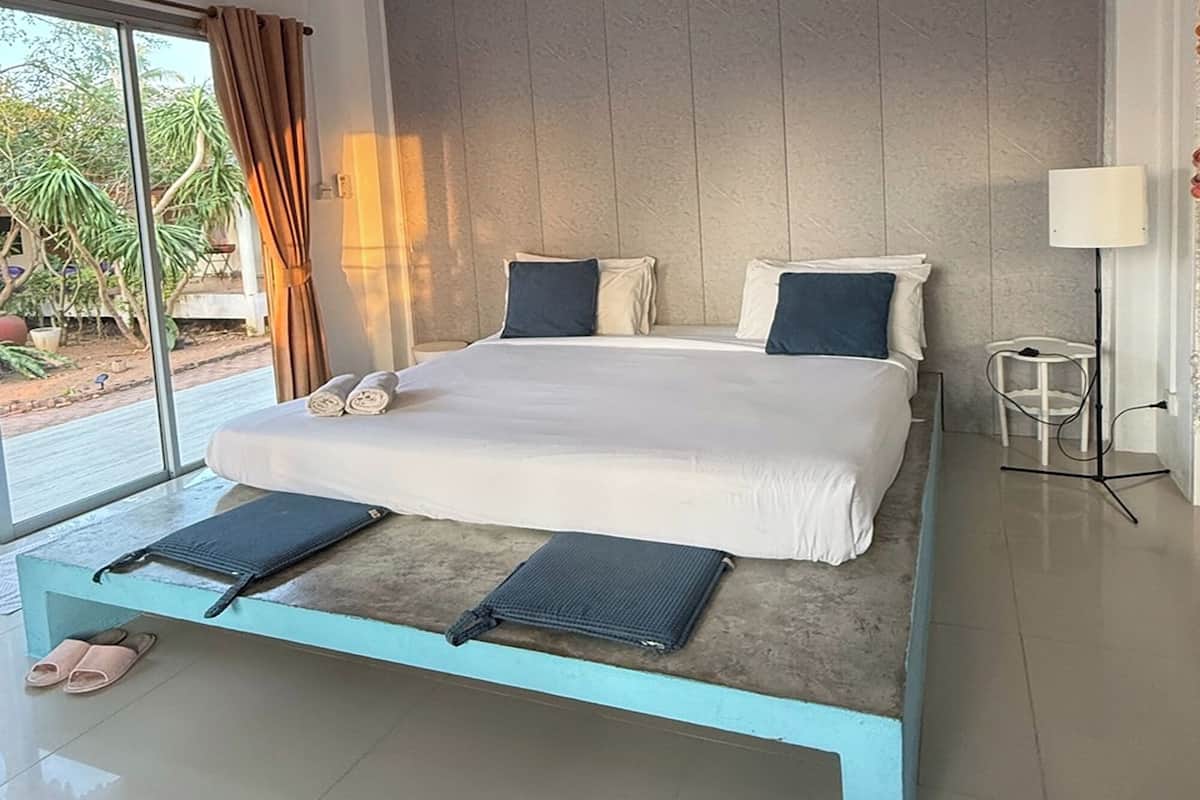 A modern bedroom with a bed, a bedside table, a lamp, and a view of the outdoors.
