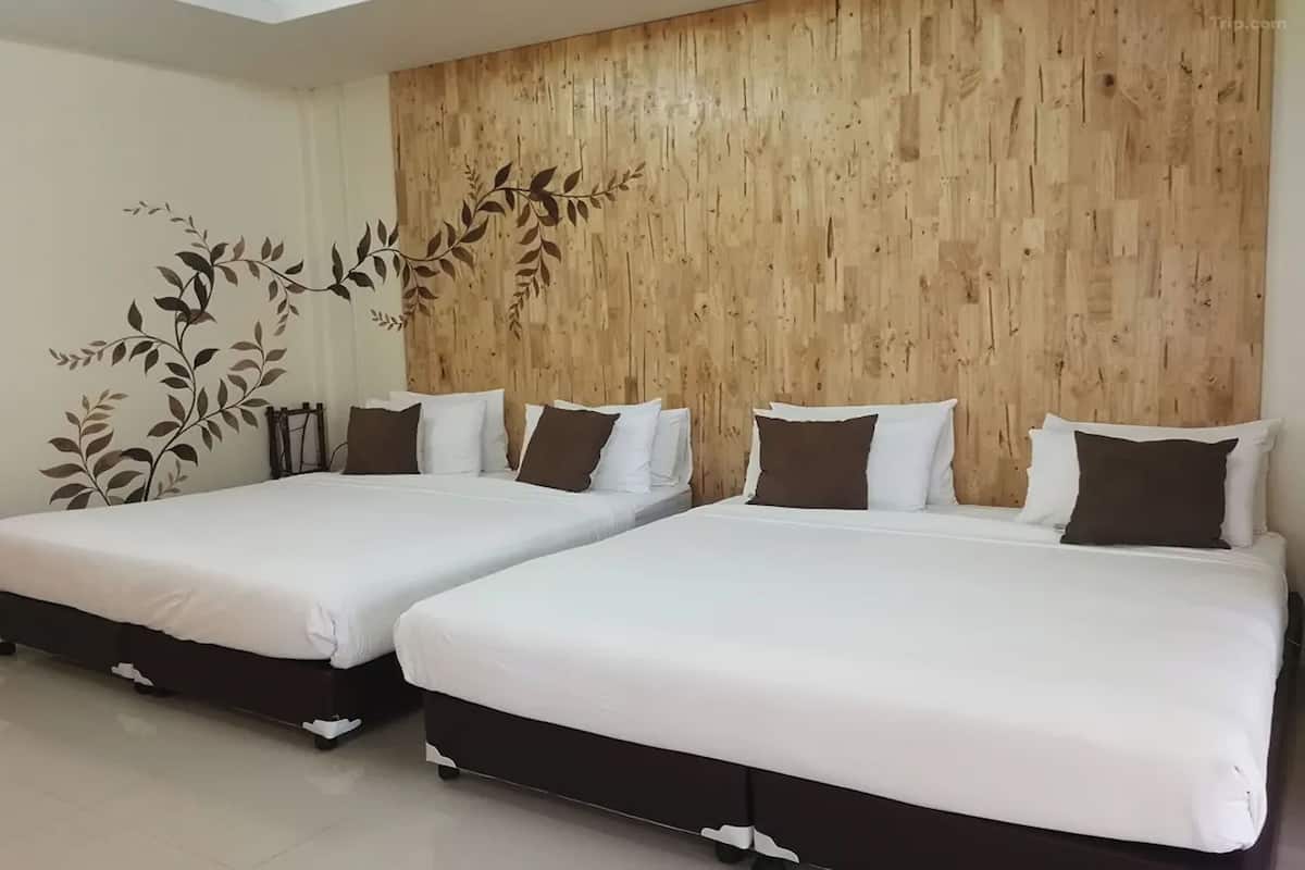A room with two beds, each with white bedding and brown pillows, against a wooden wall with a leaf pattern.