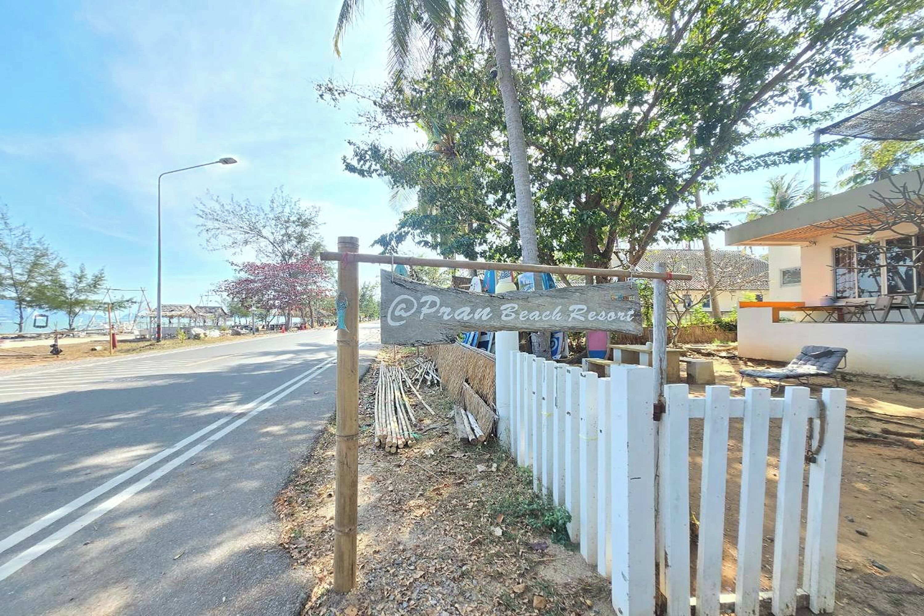 A sign for Pran Beach Resort with a white picket fence and a palm tree in the background.