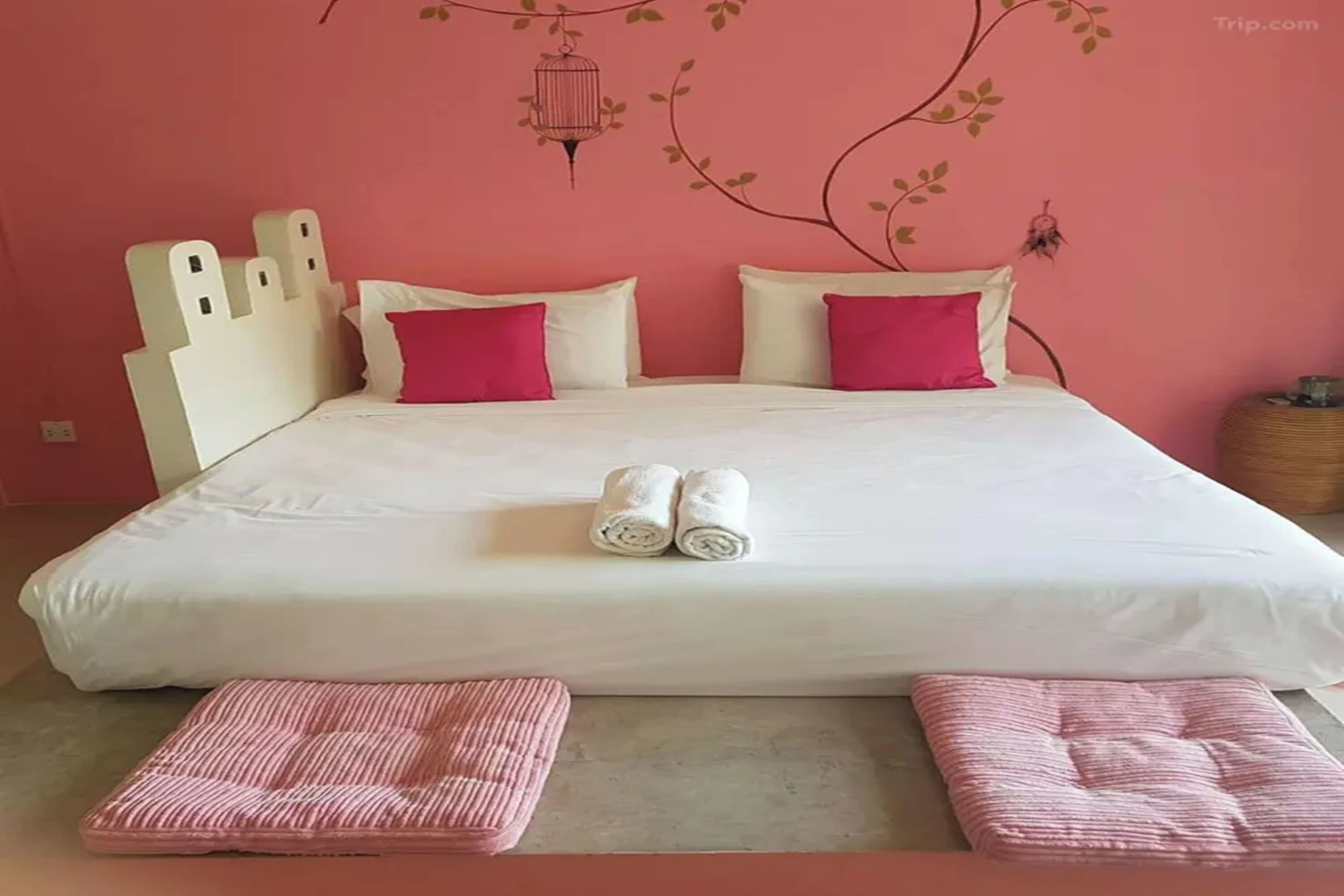 A bed with white bedding and pink pillows, a headboard with a castle-like design, and a wall with a birdcage and leaf patterns.
