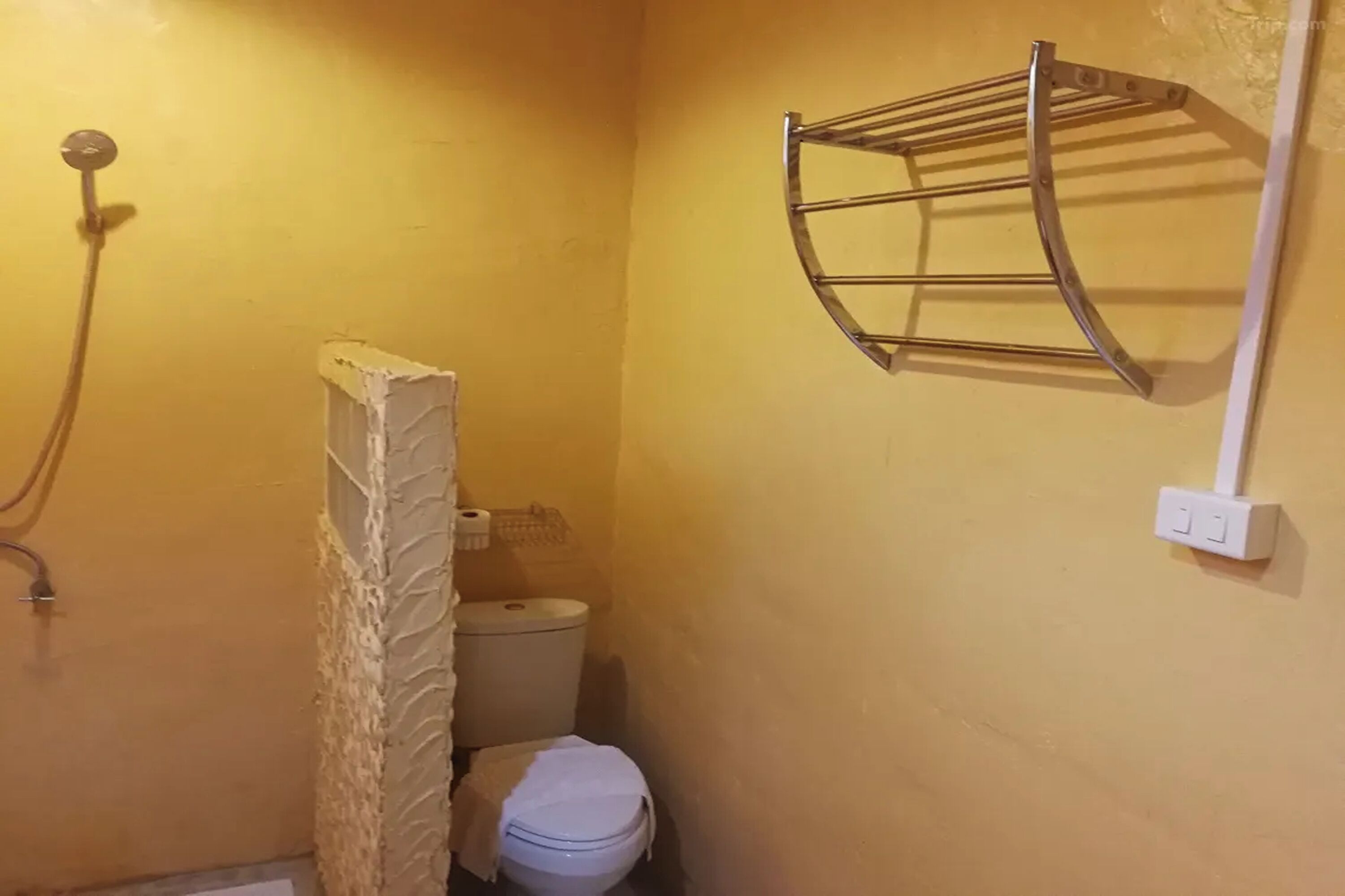 Et lille badeværelse med bruser, toilet og et håndklædetørrestativ på væggen.