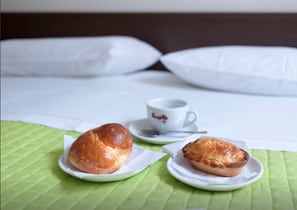 A bed with white pillows and a green bedspread. There are two plates with pastries and a cup on a saucer. - Cream & Caramel bed (Nardò)