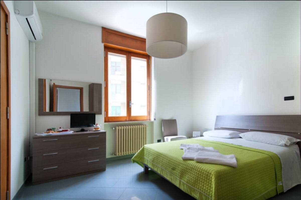 A bedroom with a bed, a dresser, a mirror, a radiator, and a window with blinds.