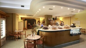 Una cafetería con un mostrador central que exhibe pastelería y un área de asientos con mesas y sillas.