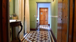 A hallway with a patterned floor, a wooden door, and a small table with a basket. - Boutique B&B Torre De' Conti (Florence)