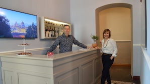 A reception area with a flat-screen TV displaying a cityscape, a bar area with bottles, and a potted plant. - Boutique B&B Torre De' Conti (Florence)