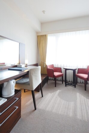 Ein Hotelzimmer mit Schreibtisch, zwei roten Stühlen, einem kleinen Tisch, einem weißen Wasserkocher und einer Minibar.
