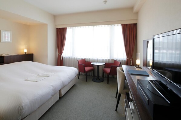 A hotel room with a large bed, a desk with a TV, a small table with chairs, and a window with curtains. - Hotel Garden Square Shizuoka (Shizuoka)
