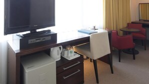 A hotel room with a flat-screen TV, a desk with a computer, a mini-fridge, and a coffee maker. There are two red chairs and a small table. - Hotel Garden Square Shizuoka (Shizuoka)