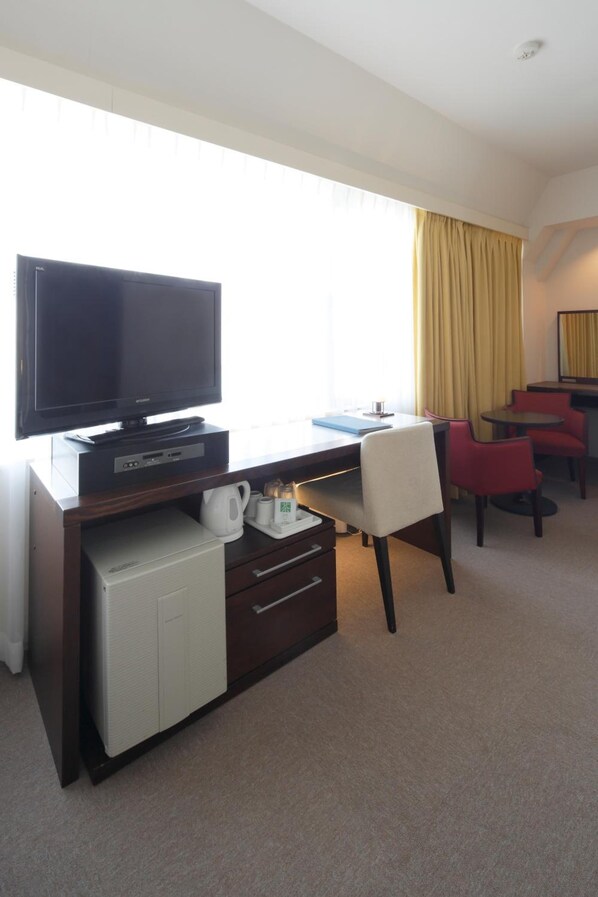 A hotel room with a flat-screen TV, a desk with a computer, a mini-fridge, and a coffee maker. There are two red chairs and a small table. - Hotel Garden Square Shizuoka (Shizuoka)