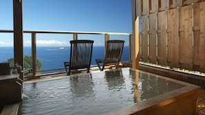 A hot tub with two chairs, a wooden fence, and a view of the ocean. - Chikurinan Mizuno (Atami)