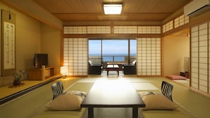 A traditional Japanese room with tatami flooring, a low table with cushions, a television, and a view of the sea. - Chikurinan Mizuno (Atami)