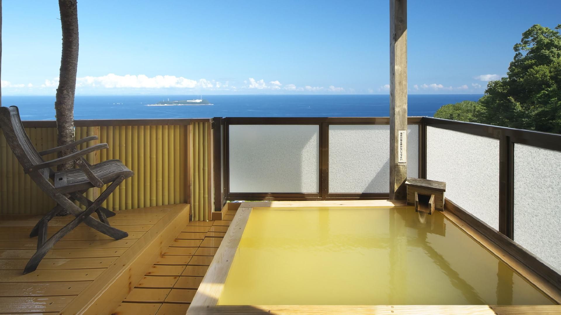 A wooden deck with a hot spring bath, a chair, and a view of the ocean.