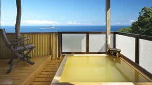 Um deck de madeira com banheira de águas termais, uma cadeira e vista para o oceano.