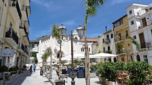 A sunny street with buildings, outdoor seating, and a palm tree. - Caudullo (Letojanni)