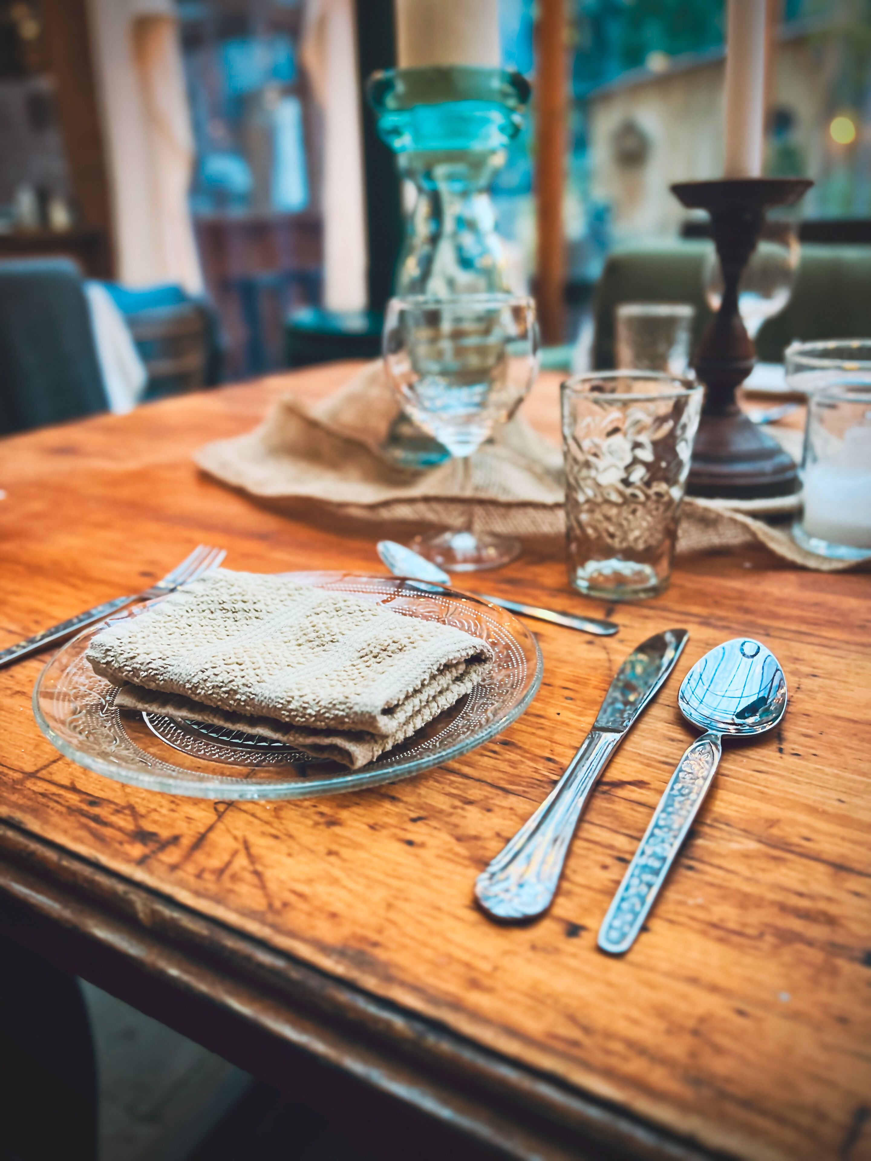 Una mesa de madera dispuesta con un mantel doblado, un plato de vidrio, cubiertos y un candelabro.