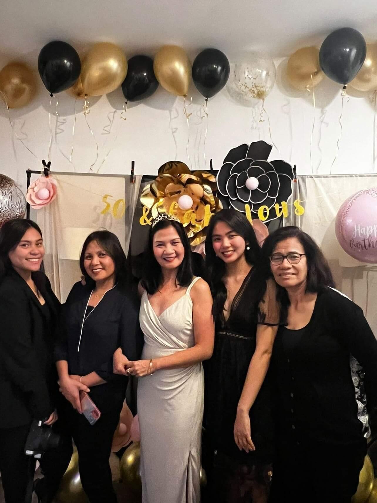 A group of people at a party with balloons and a large flower decoration.
