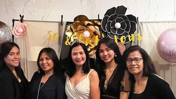 A group of people at a party with balloons and a large flower decoration.