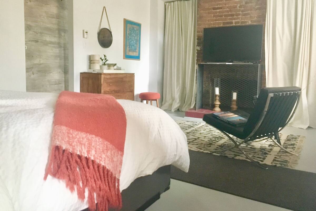 A bedroom with a bed, a fireplace, a TV, and a chair.