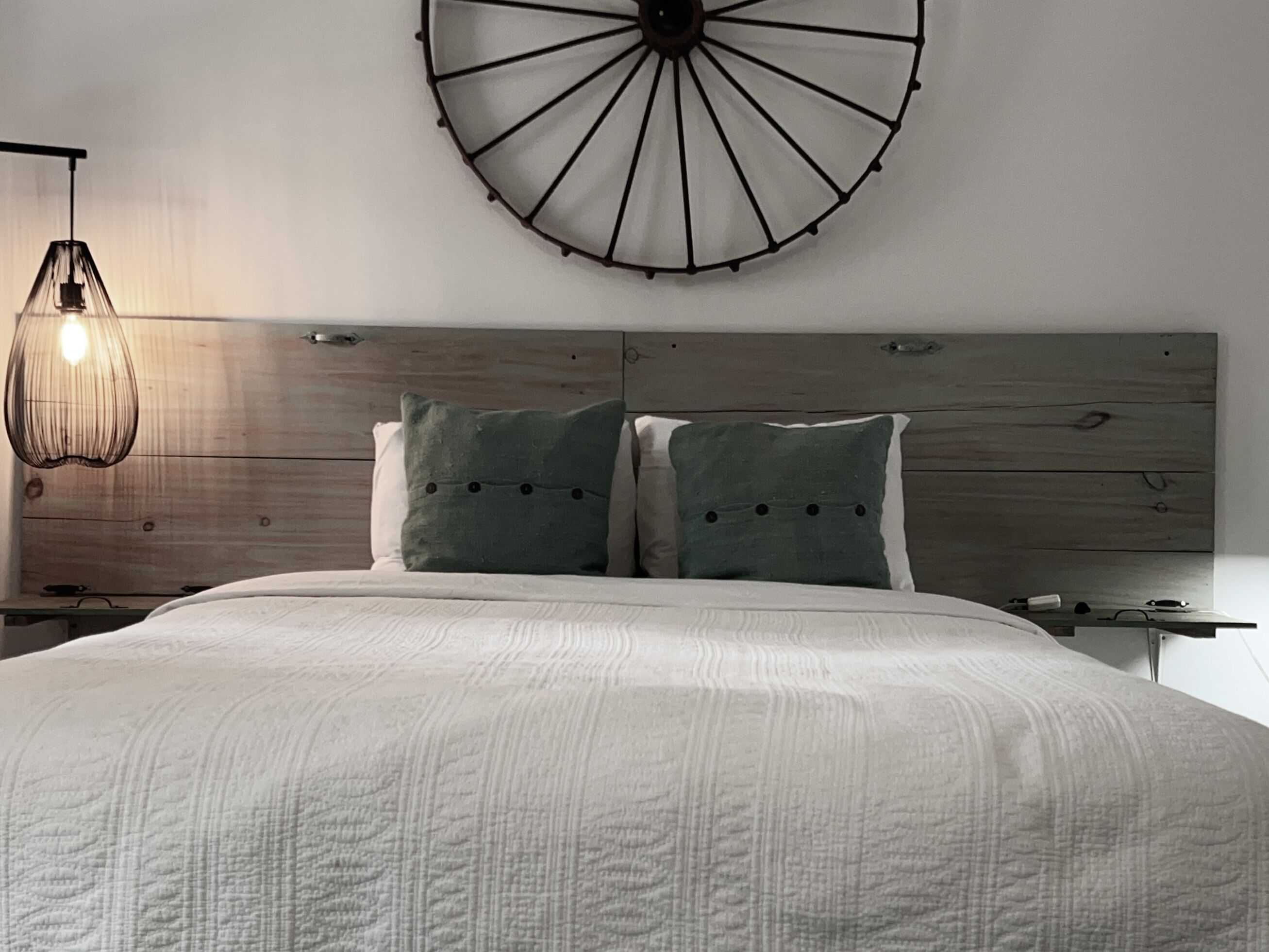 Une chambre avec un grand lit, deux oreillers, une tête de lit en bois, un luminaire circulaire fixé au mur et un autre luminaire suspendu au plafond.