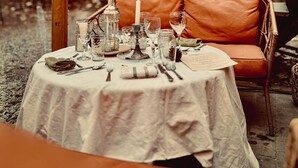 An outdoor dining area with a round table set for a meal, wooden beams overhead, and a cushioned bench. - HPG Griffintown (Montreal)