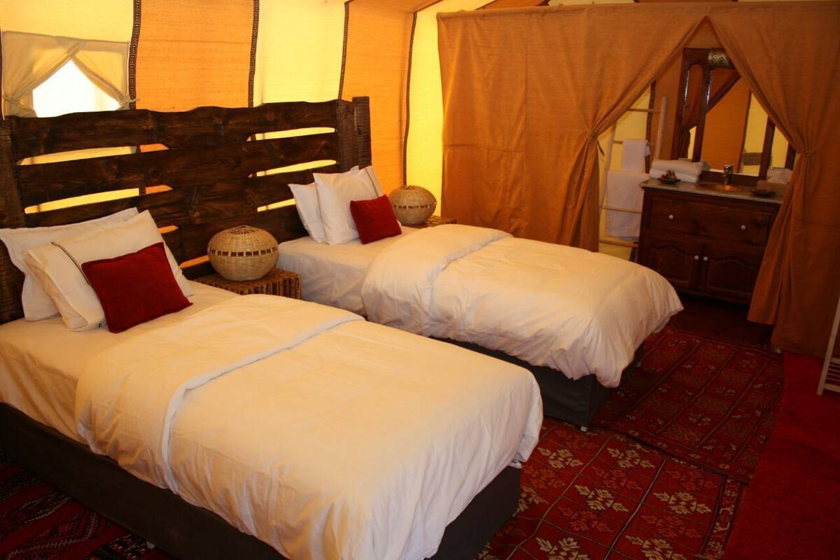 A room with two beds, a wooden headboard, a mirror, a dresser, and a patterned carpet.