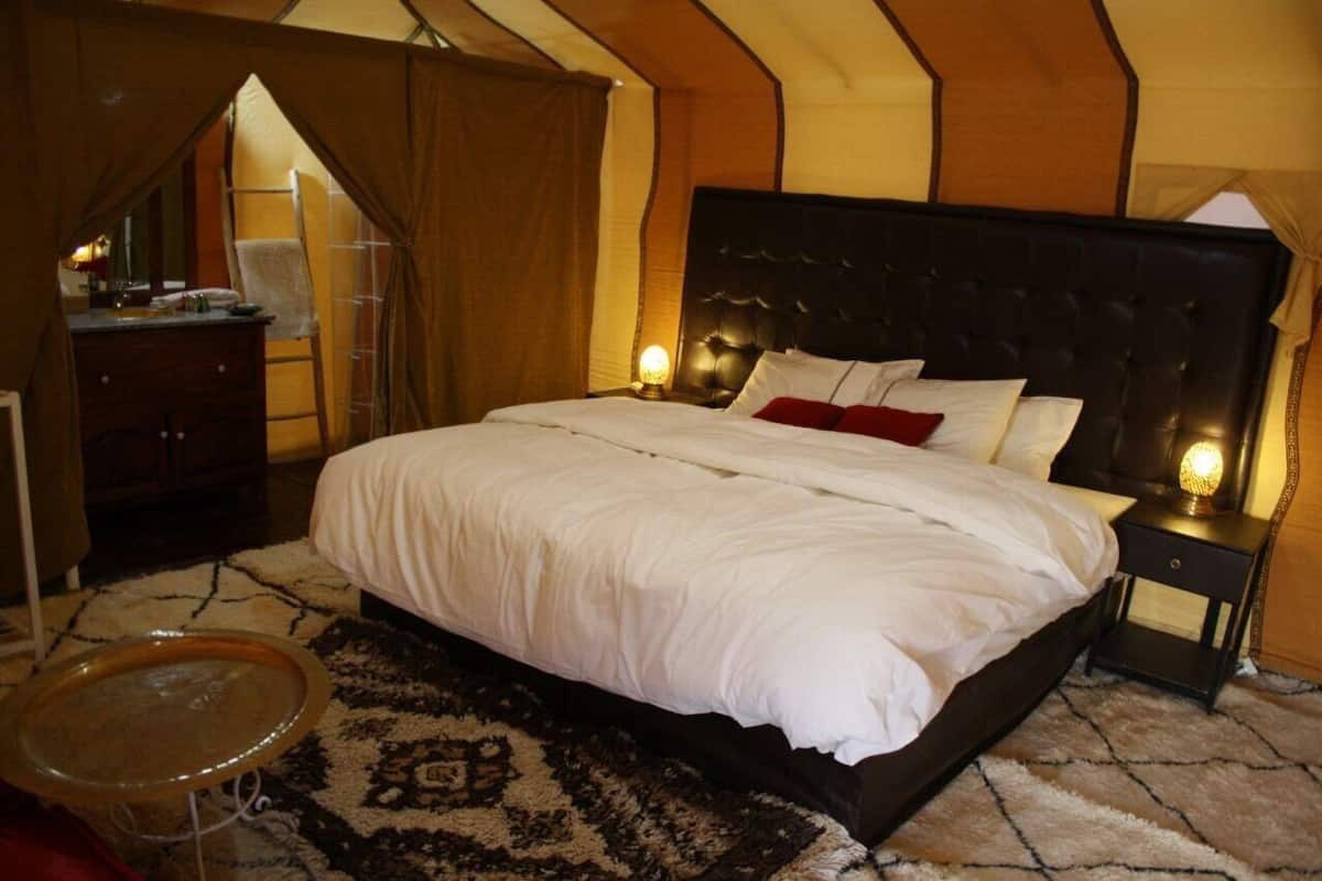 A bedroom with a large bed, a nightstand, a lamp, a dresser, and a small round table.