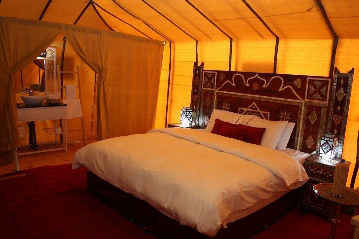 A tent-style room with a bed, a small table, and a sink.