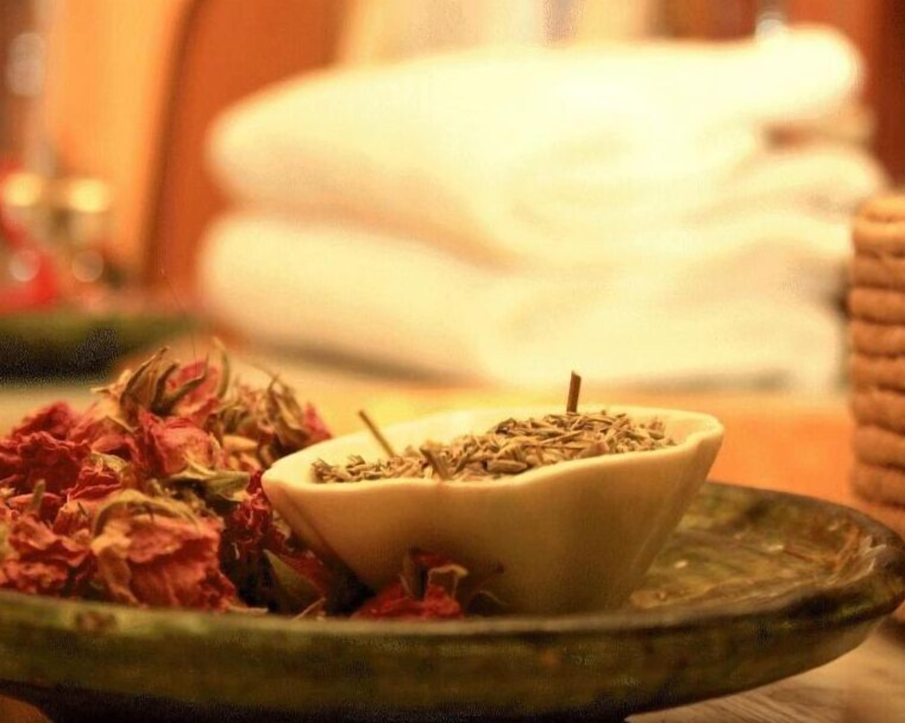 Un cuenco de hierbas secas sobre un plato, con un montón de flores secas a un lado.
