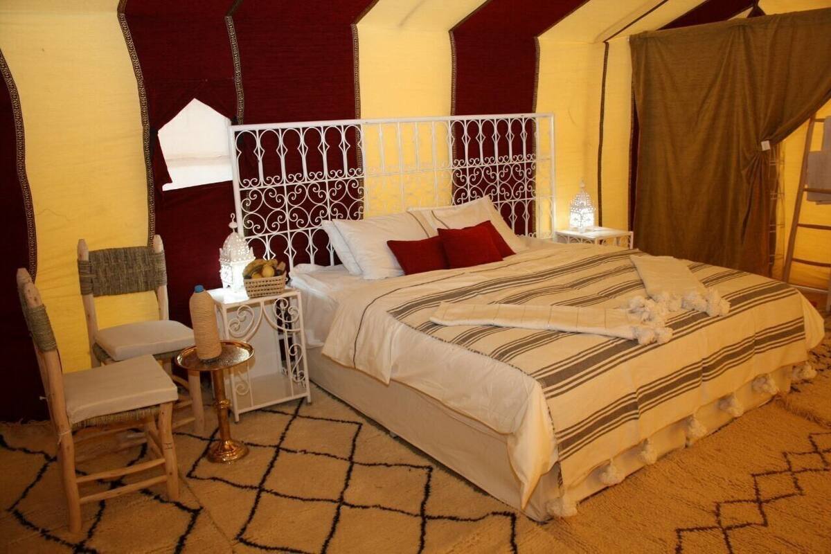A bedroom with a bed, a chair, a small table, and a decorative headboard.