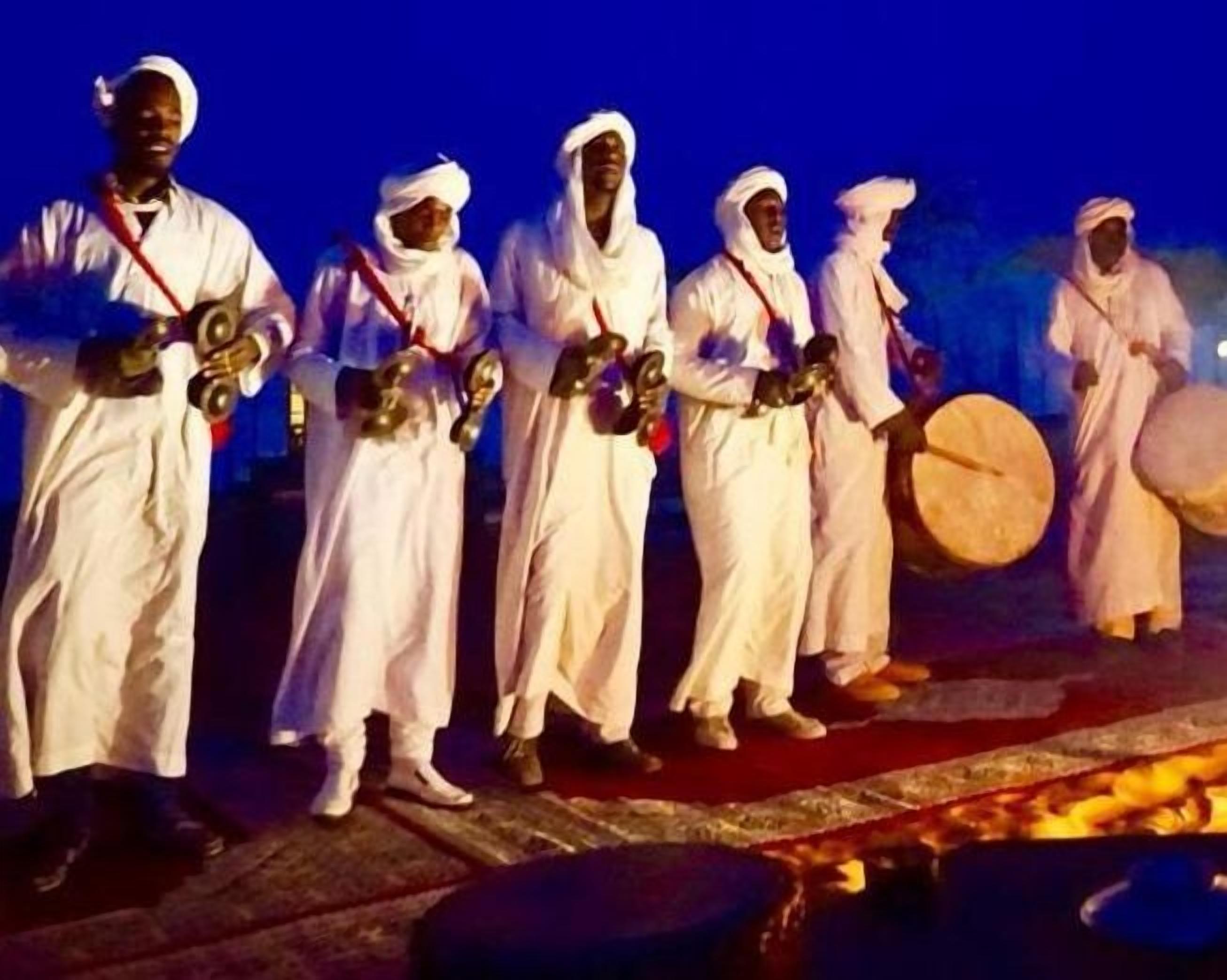 A group of people in white traditional attire standing on a stage with musical instruments.