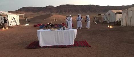 Campa en el desierto con tiendas de campaña, una mesa dispuesta para una comida y montañas al fondo.